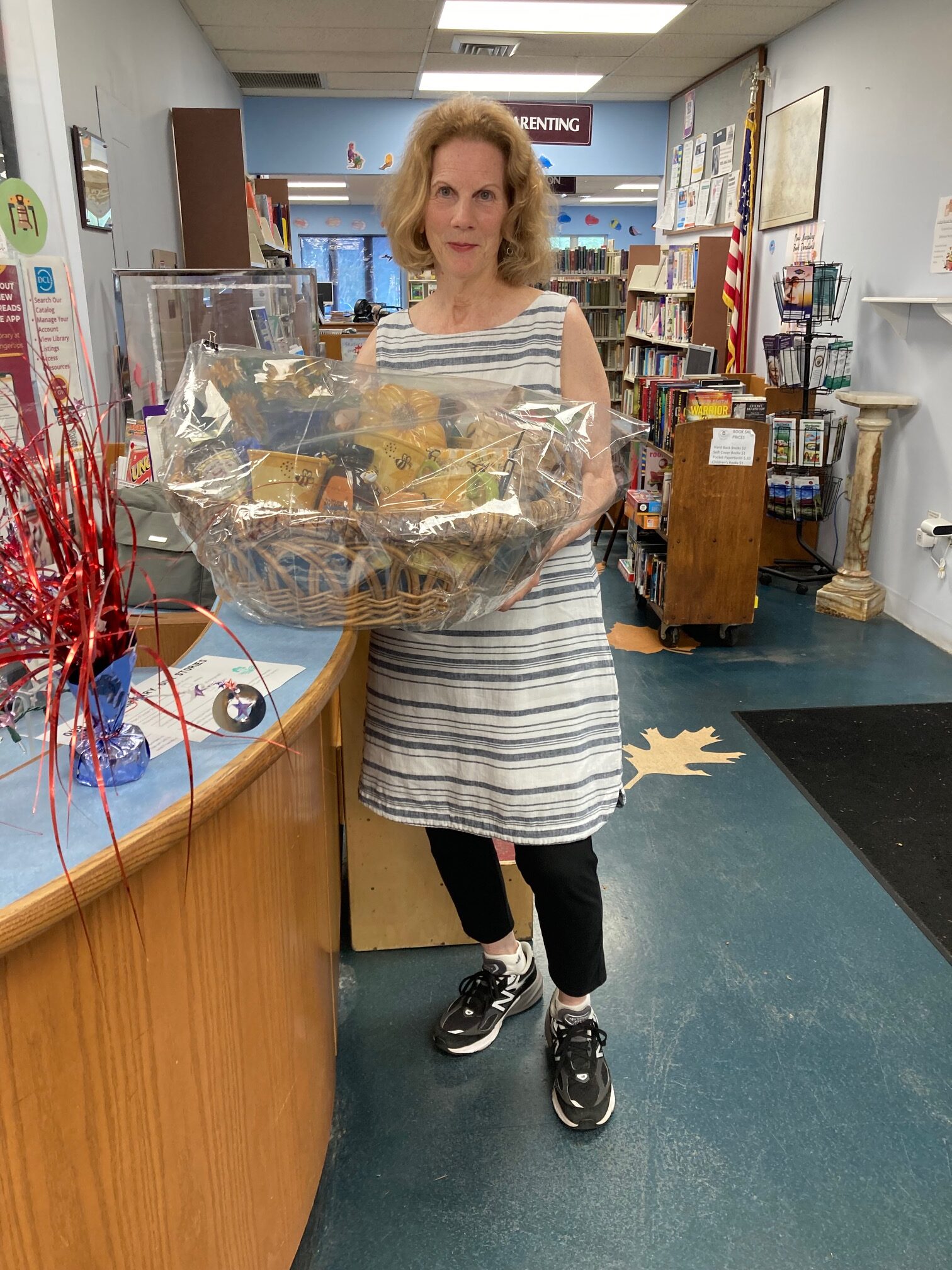 A woman standing in the library holding the Raffle Basket that she won.